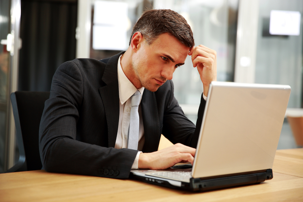 Confident businessman sitting with laptop at office Feeling Overwhelmed with Your Social Media Accounts?