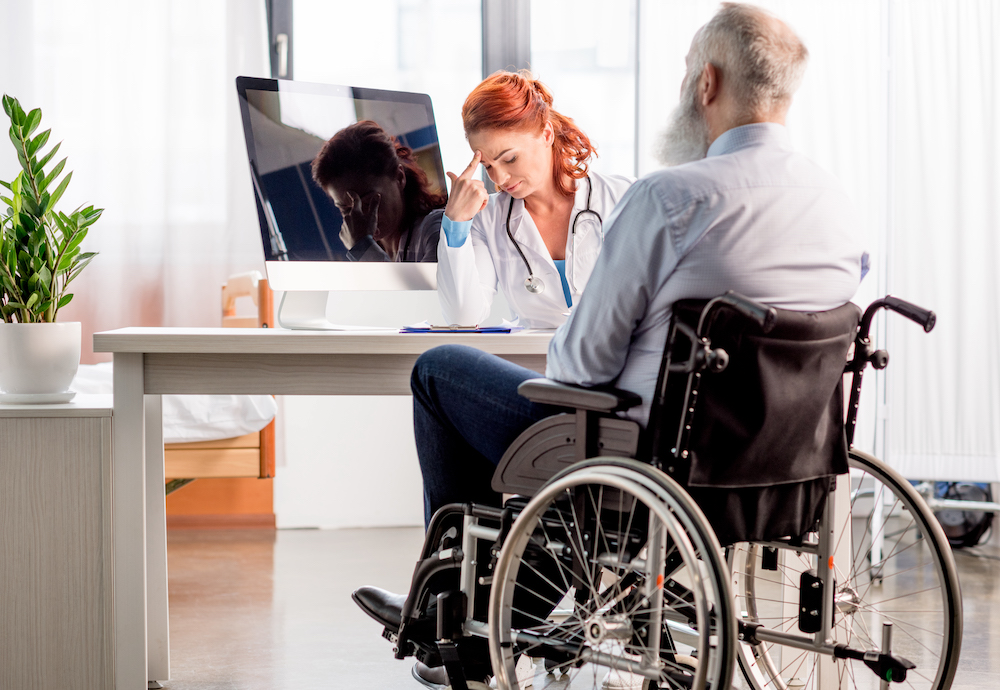 Back view of senior man in wheelchair consulting with concentrated female doctor